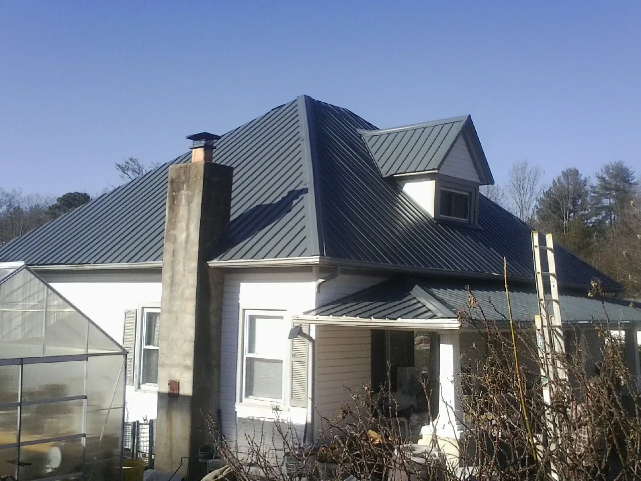 Dark blue standing seam metal roof on a white farmhouse with dormer — Slate & Tile Roof Repair by Roofing Brothers in Toronto