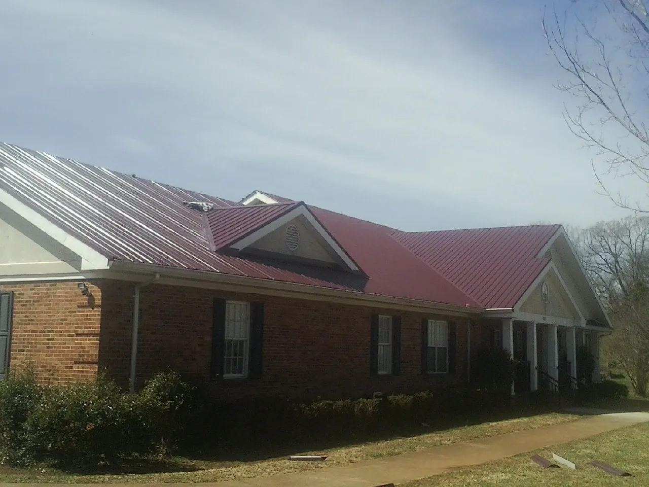 Red metal roof with gabled entries on a long brick building, from a Hail Damage Roof Repair job in Toronto