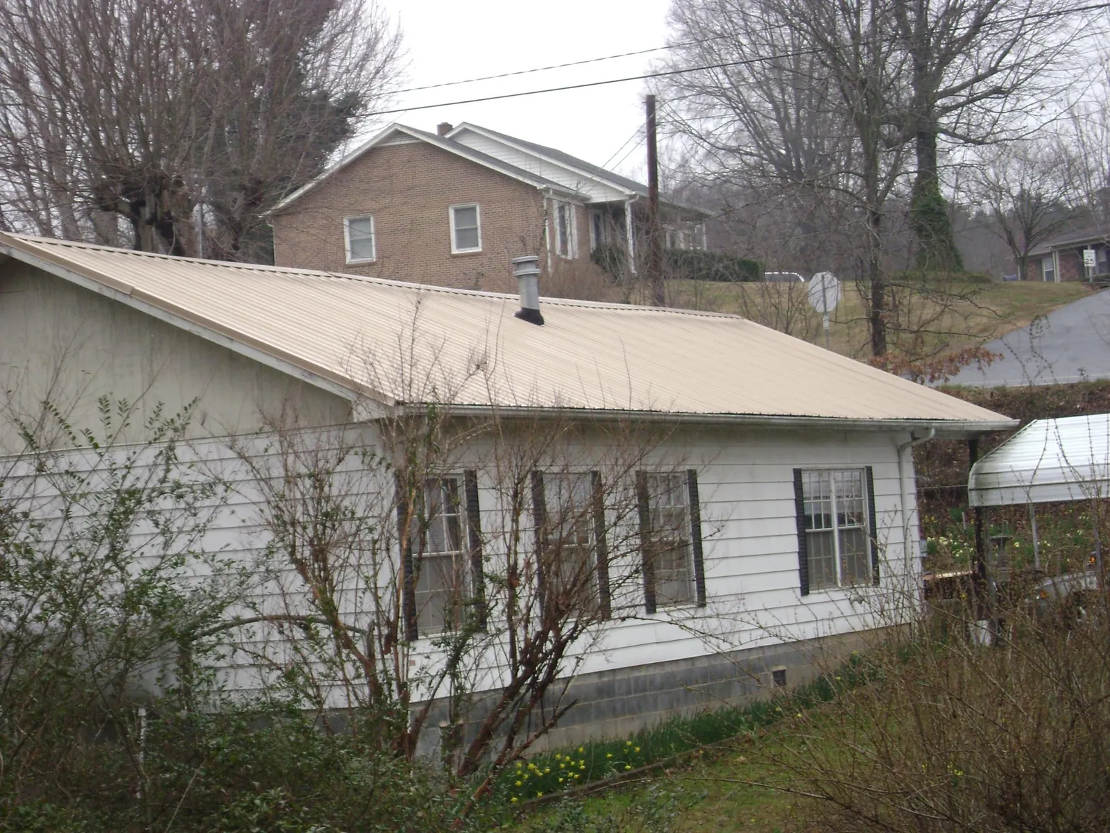 Tan metal roof on a white sided house set into a hillside — Commercial Roofing by Roofing Brothers in Toronto